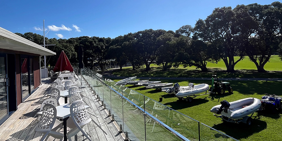 Outdoor deck with white chairs and tables overlooking lawn and boats