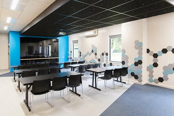 Meeting room with rows of black tables and chairs, projection screen, and hexagon wall graphics