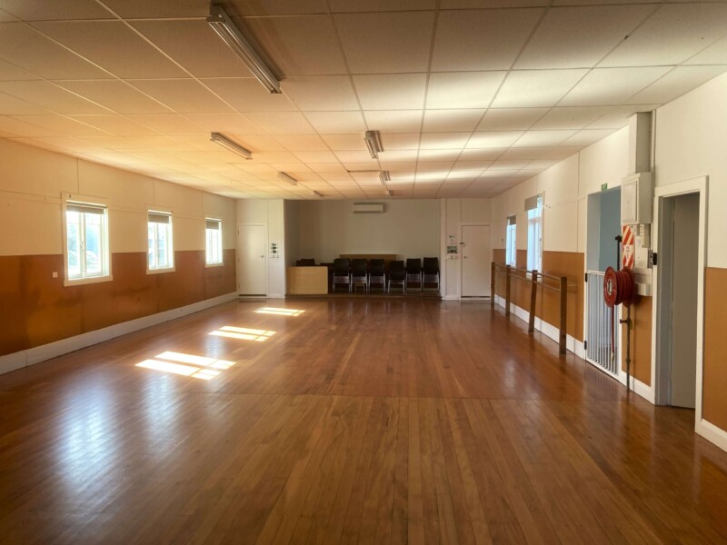 Open hall with timber floor, strip lighting and chairs stacked at rear