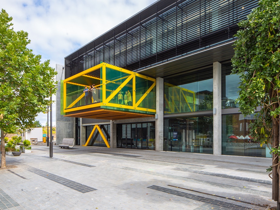 Contemporary building with yellow steel canopy box, concrete pillars, and glazed facade, urban setting