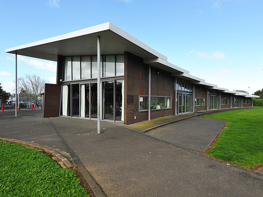 Side view of low-rise community centre building with canopy, large windows, and lawn