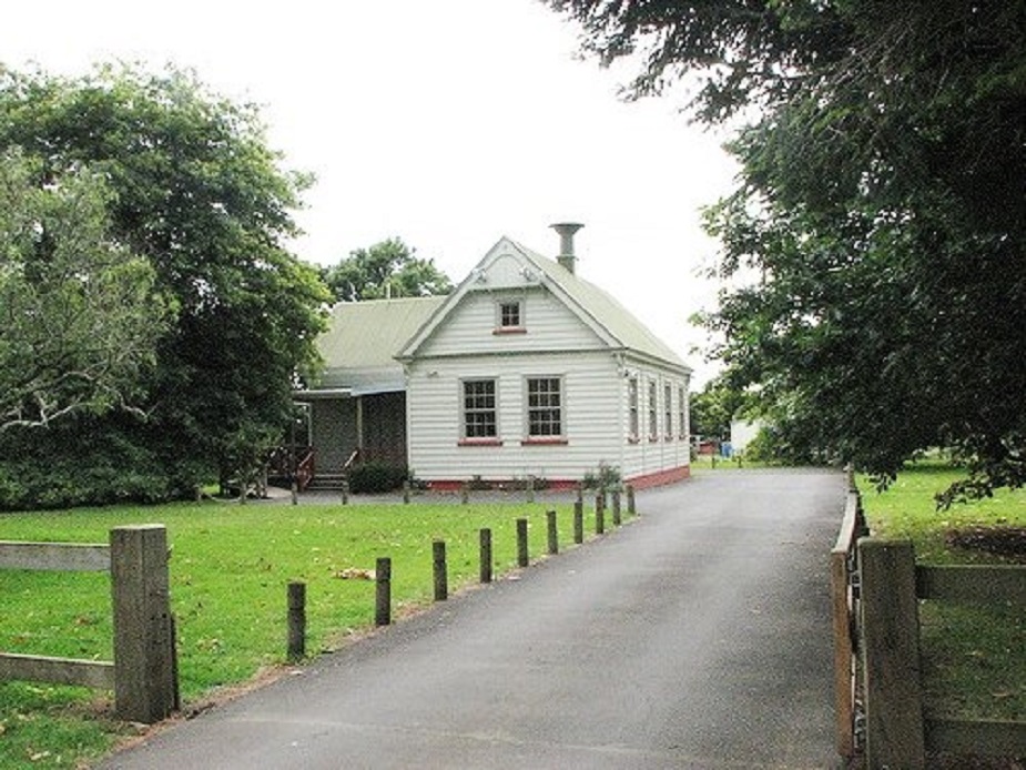 Heritage wooden hall with gabled roof approached by a driveway through trees