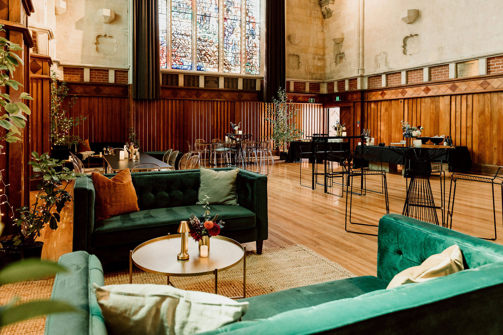 Historic hall interior with dark timber panelling, stained glass windows and lounge seating