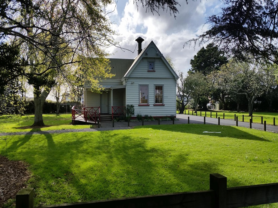 Small heritage villa-style hall with verandah set on a lawn surrounded by trees