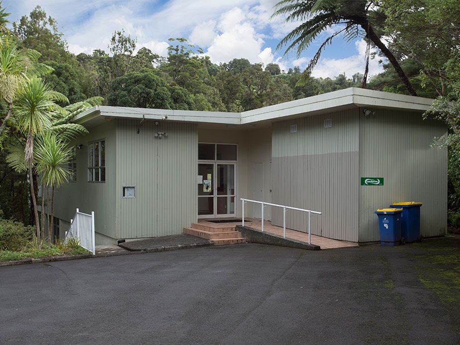 Single-storey community hall with vertical cladding and access ramp surrounded by trees