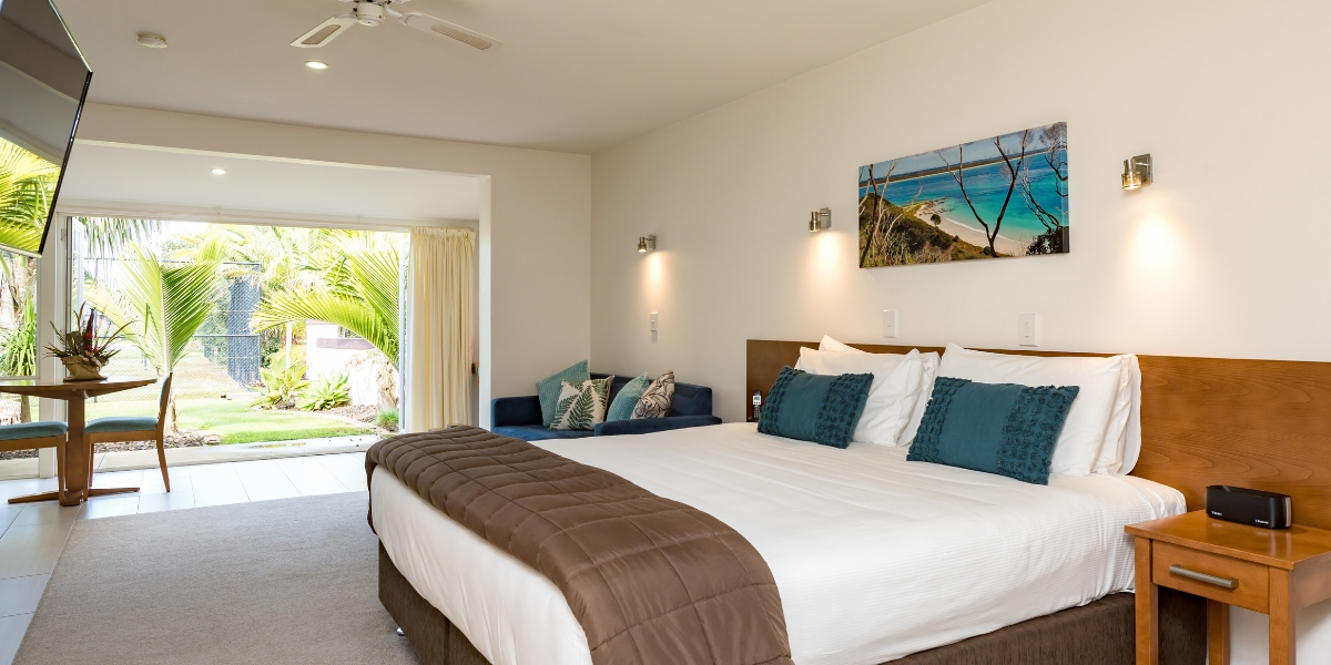 King bedroom with teal cushions, wall art, and sliding doors to garden terrace
