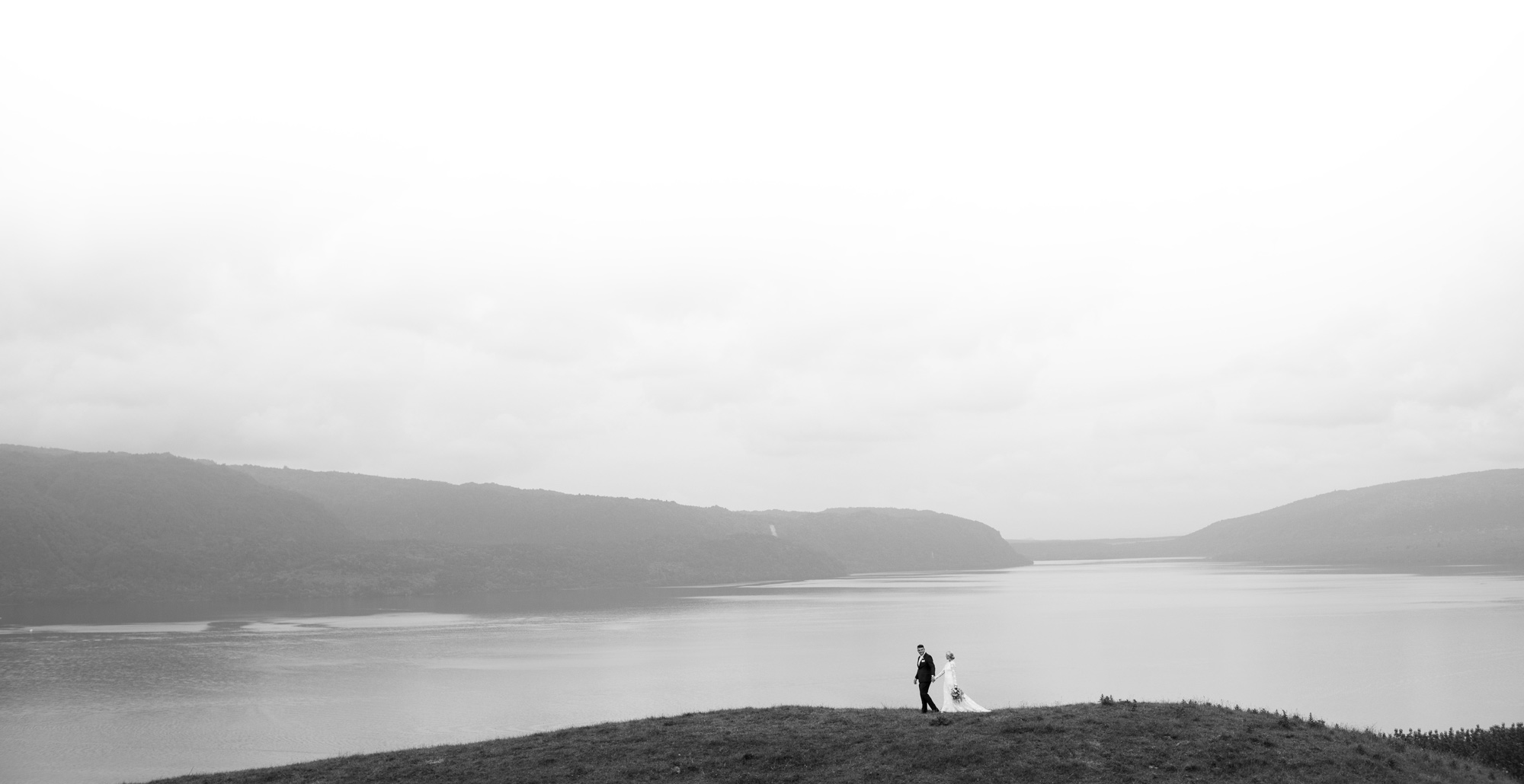 Two figures on grassy hillside beside a lake with misty hills, black and white landscape