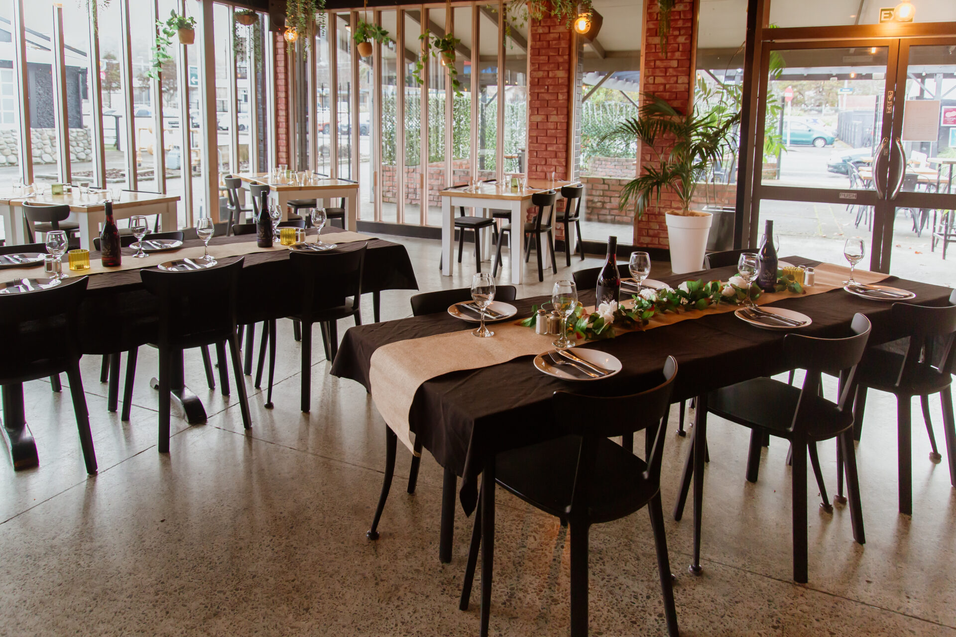 Brick and glass dining room with set long tables, concrete floor, and street view