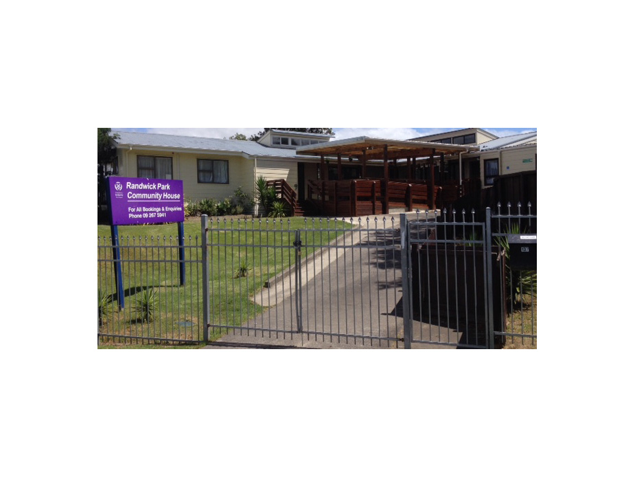 Single-storey community house behind iron fence with signage and covered deck