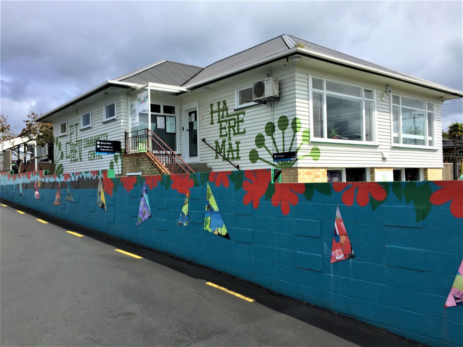 Single-storey white weatherboard community centre with colourful mural on boundary wall