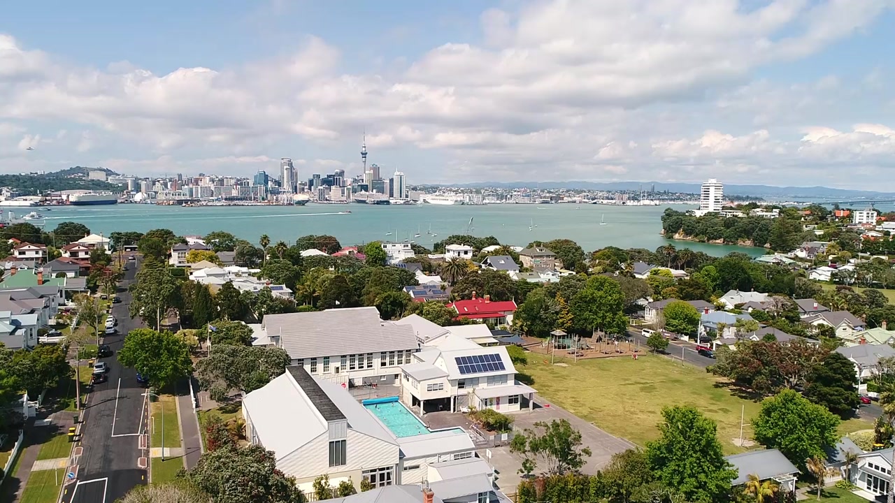 Aerial view of school buildings and pool with harbour and city skyline behind