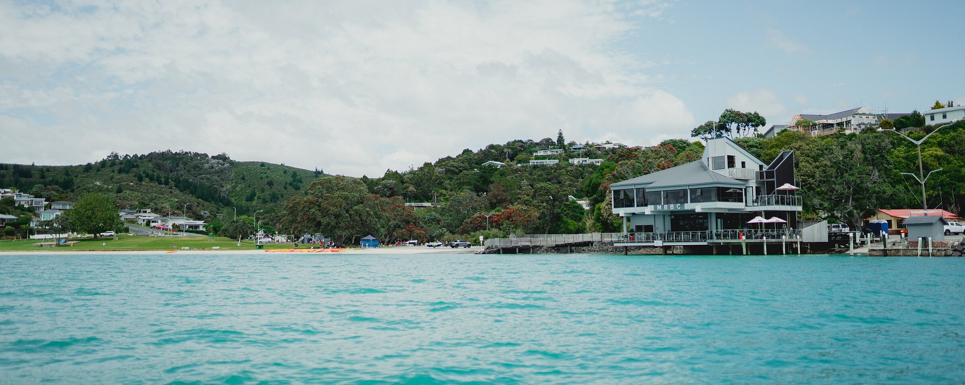 Two-storey club building on waterfront viewed from the water with hills behind