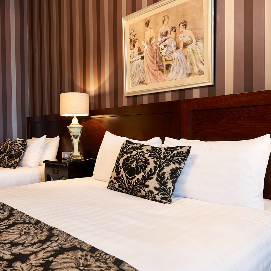 Hotel room with two double beds, striped wallpaper and framed artwork