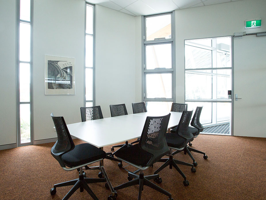 White meeting room with long white table, black chairs, tall narrow windows and artwork