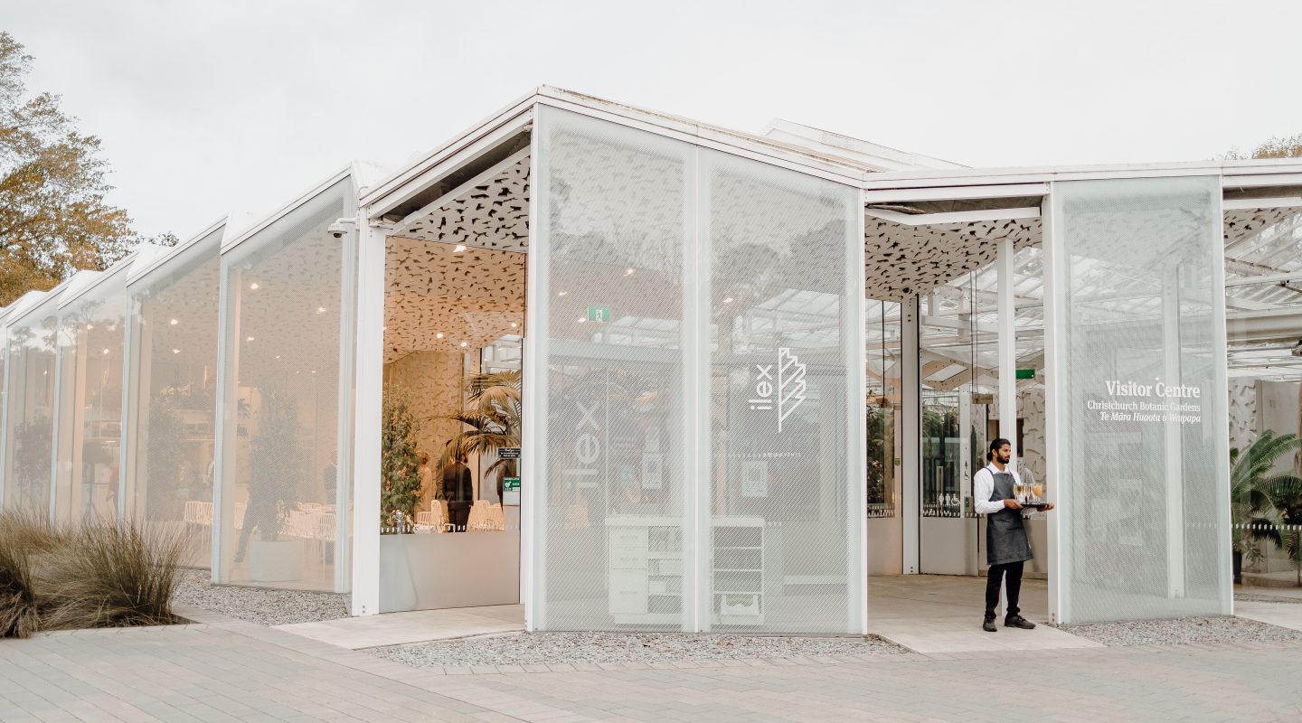 White glazed pavilion exterior with perforated roof panels, timber columns and gravel surrounds