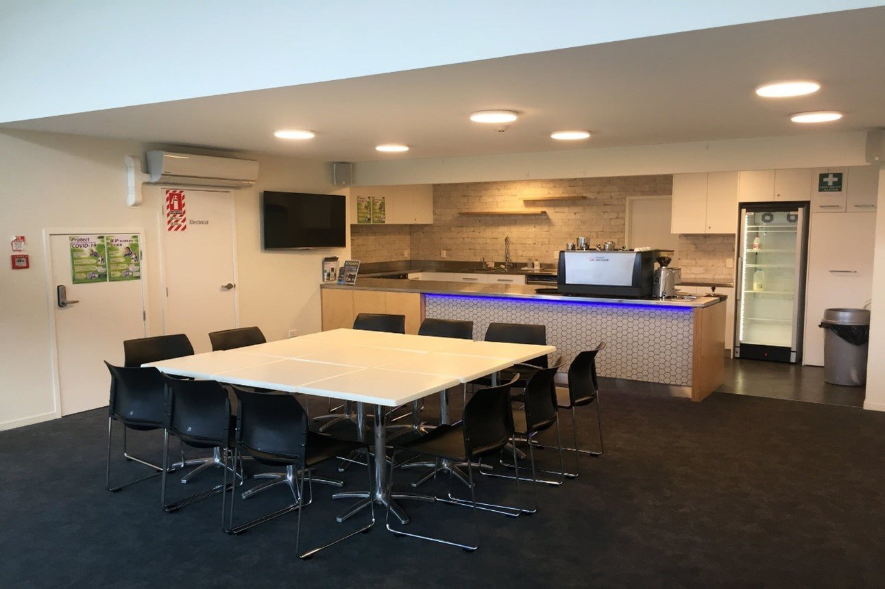Small room with a white table, dark chairs, kitchen counter with appliances, and a TV on the wall