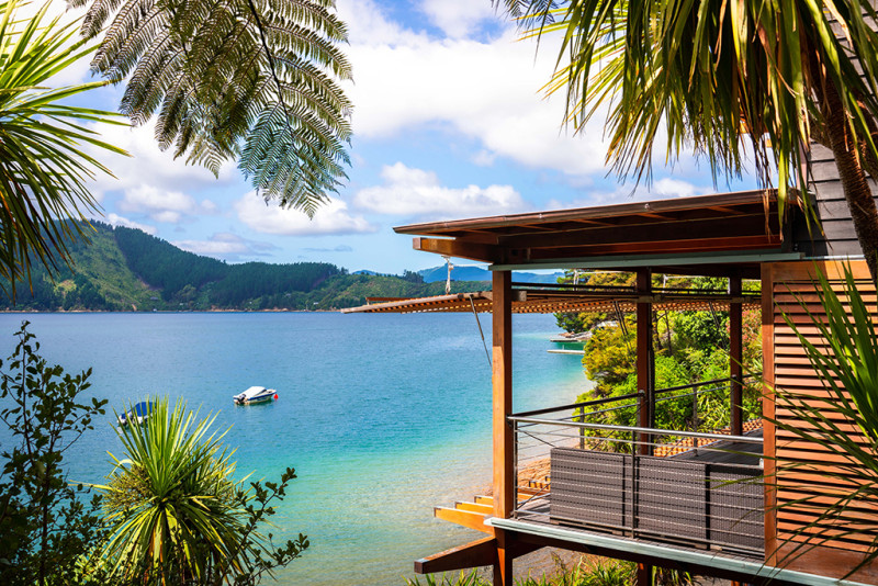 Waterfront timber lodge building with a deck and jetty, surrounded by native bush and a sheltered cove