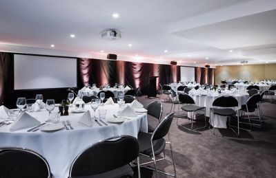 Banquet room set with round tables, white napkins, and projection screen