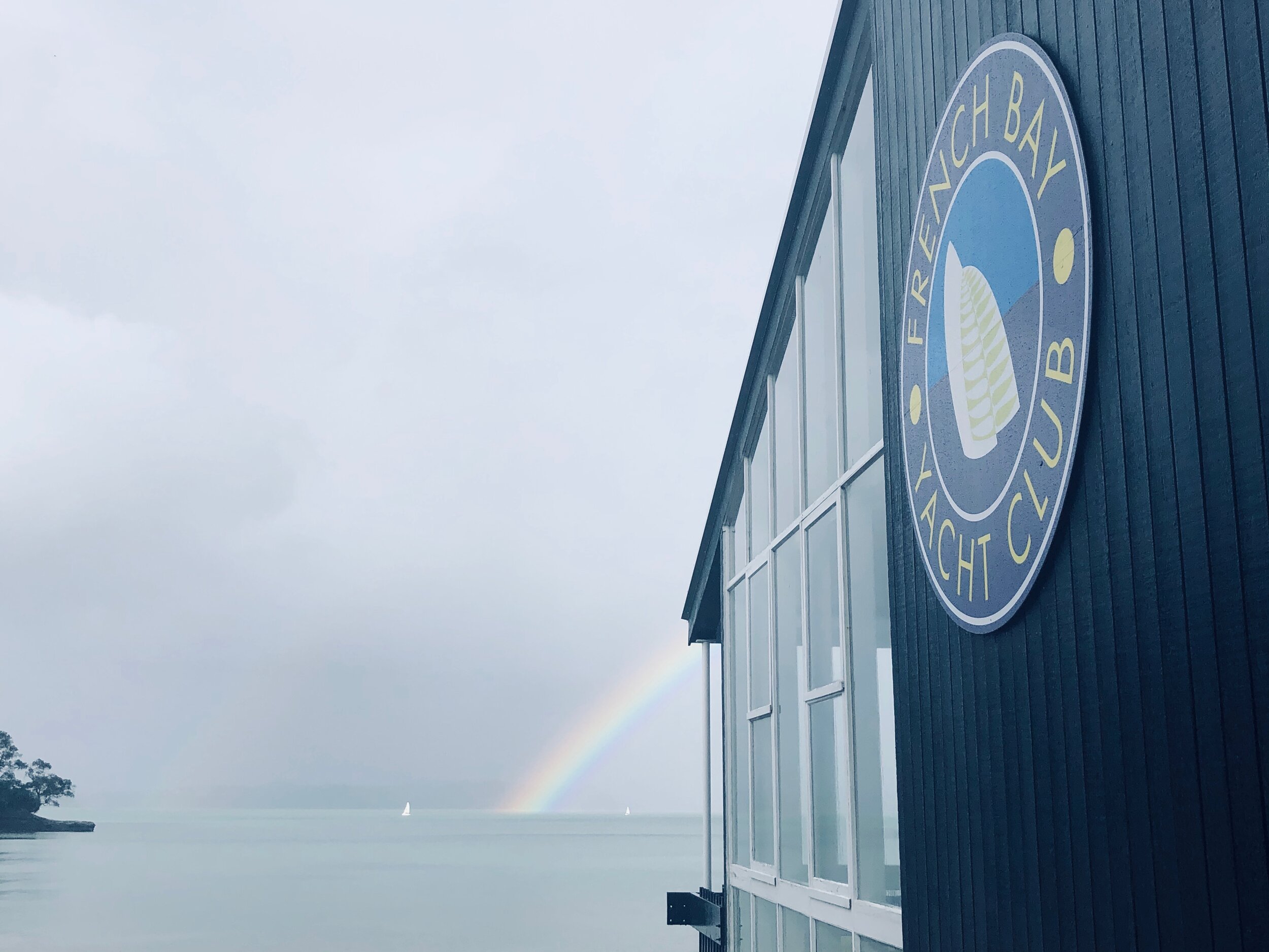 Dark blue clubhouse exterior with circular logo and rainbow over water