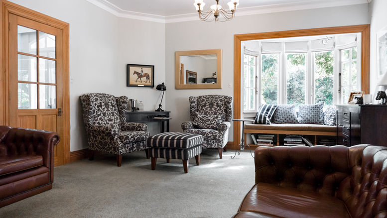 Homestead sitting room with a leather Chesterfield sofa, wingback chairs and a bay window