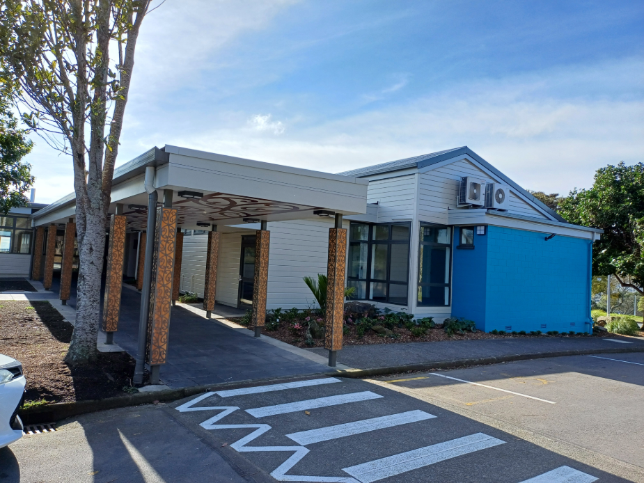 White weatherboard building with a covered canopy entrance featuring patterned carved posts