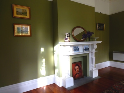 Period room with white fireplace surround, framed paintings, and olive-green walls