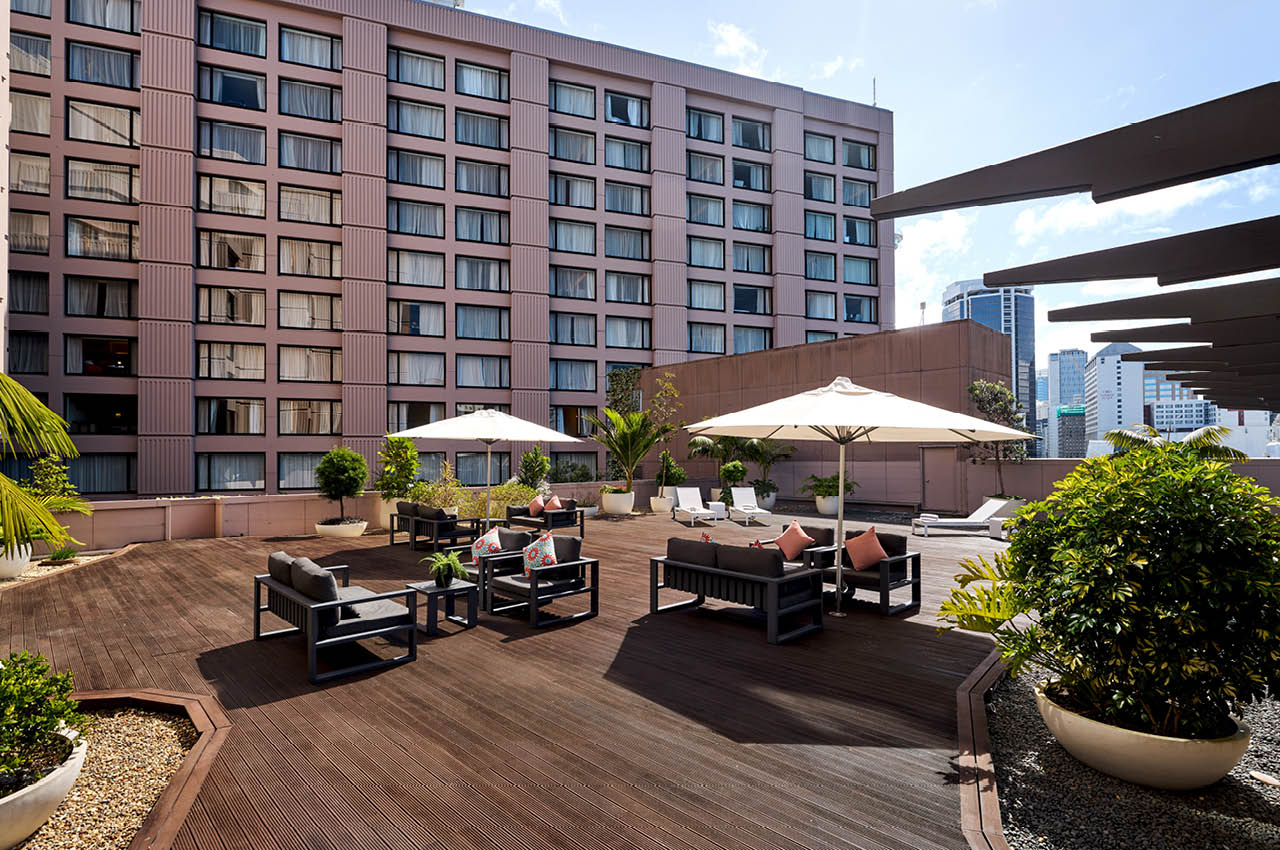 Elevated outdoor timber deck with lounge furniture, white umbrellas, and city buildings behind