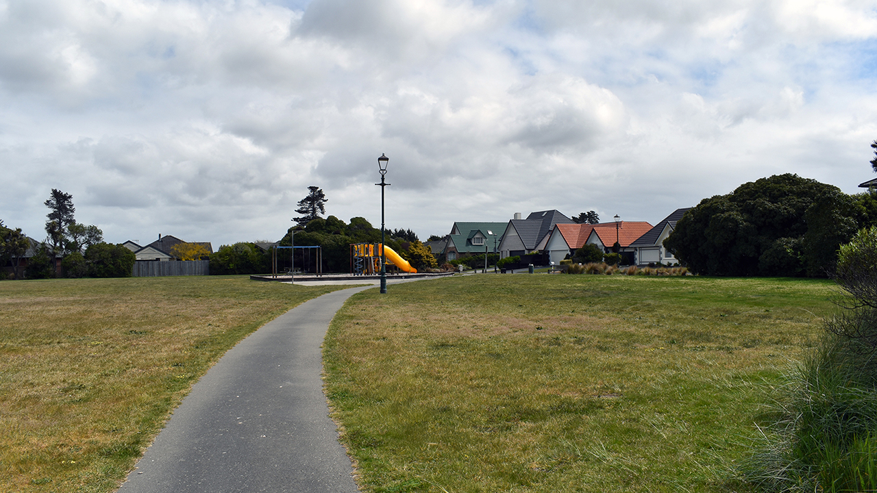 Open park with path, playground equipment and surrounding houses