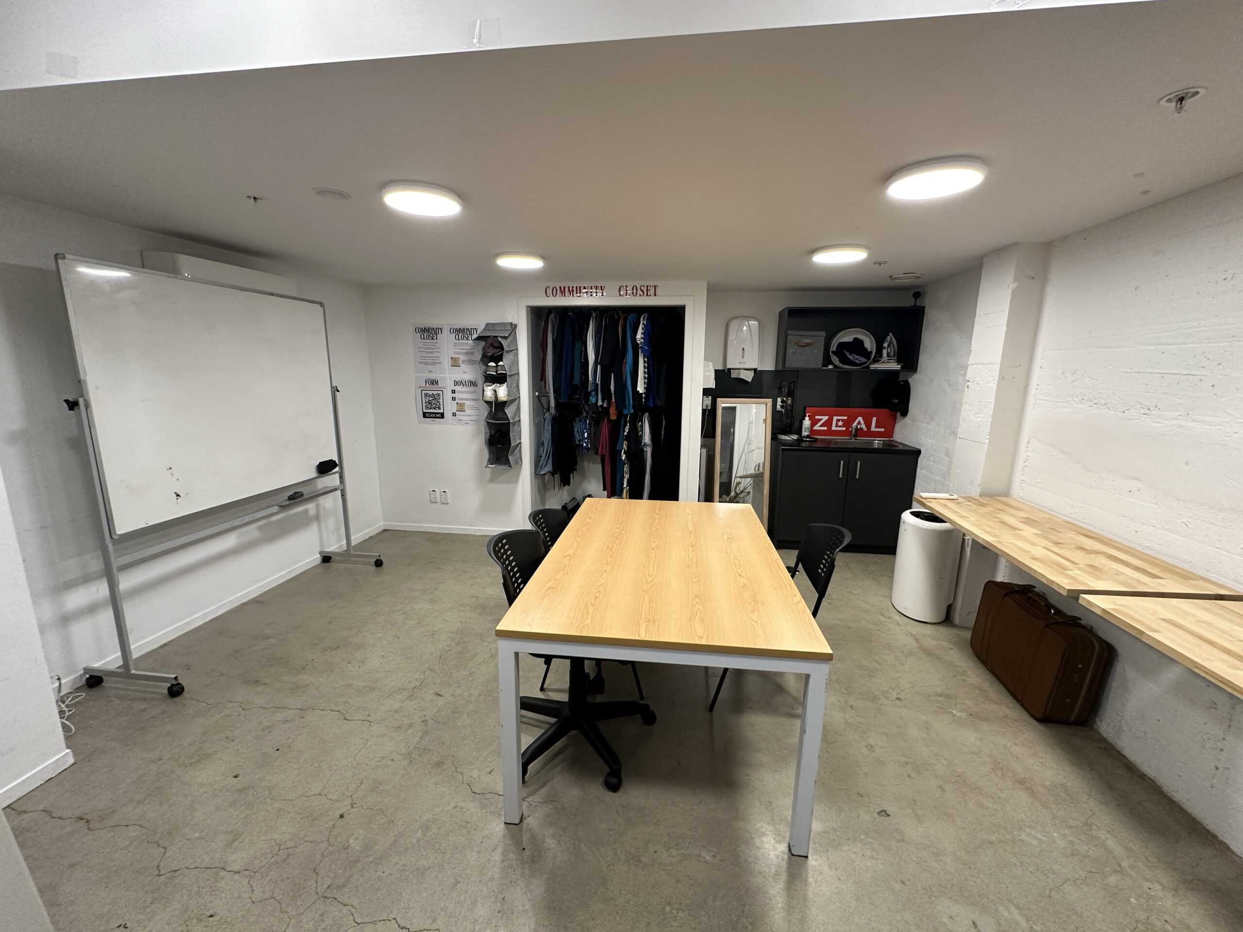 Plain concrete-floored room with whiteboard, timber table and clothing rail