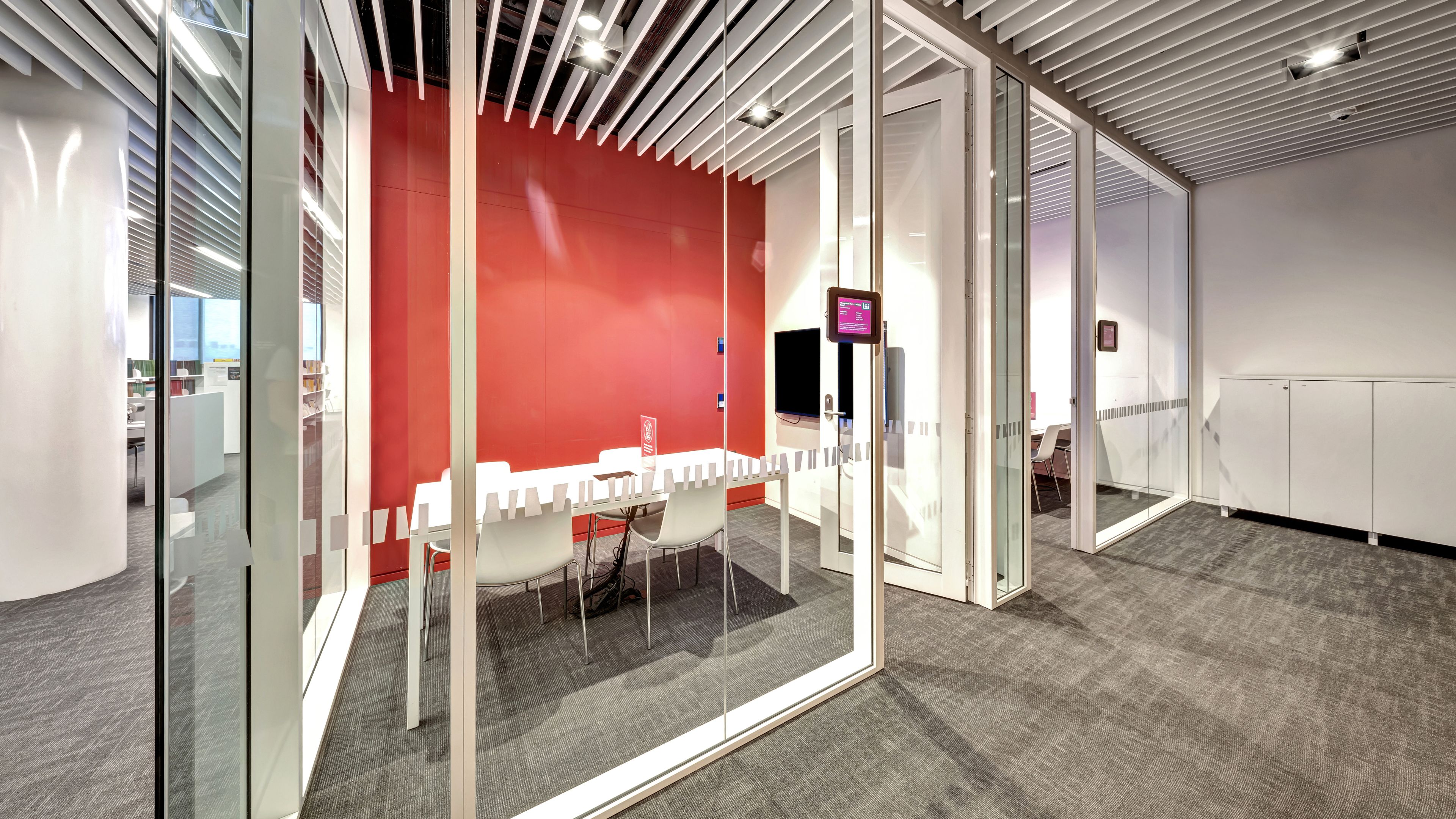 Glass-walled meeting room with red feature wall, table and white chairs