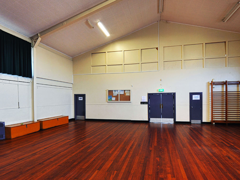 Empty hall with vaulted ceiling, polished timber floor, and curtained stage
