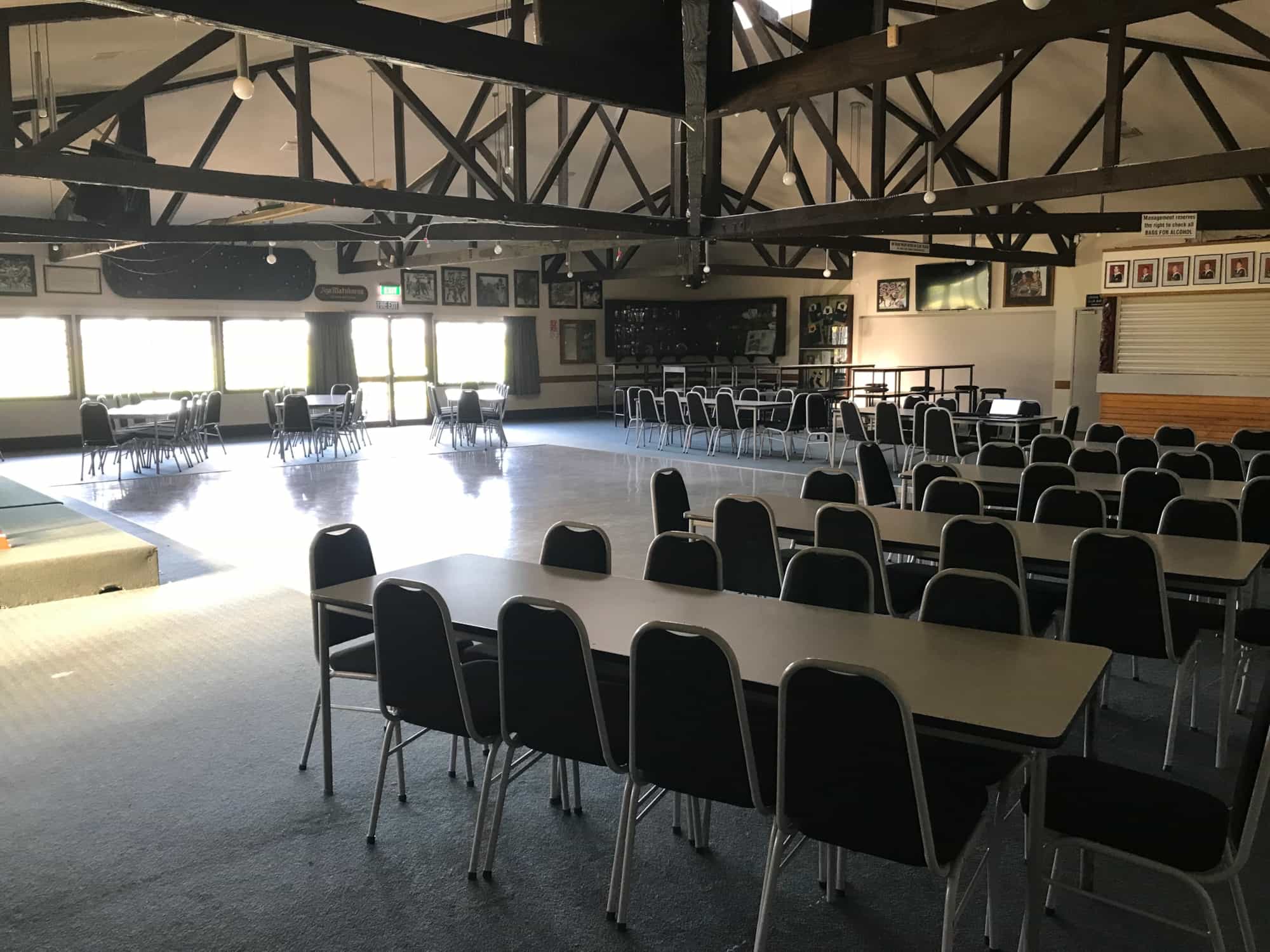 Club hall with dark timber roof trusses, tables and chairs, and framed photos on walls