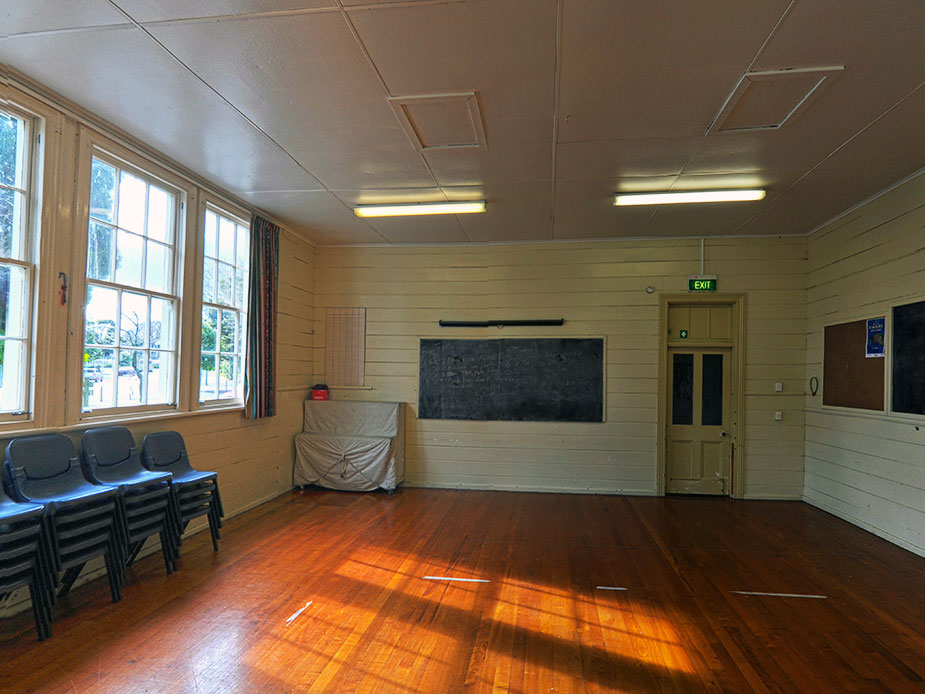 Timber-floored hall interior with stacked chairs and chalkboard on wall