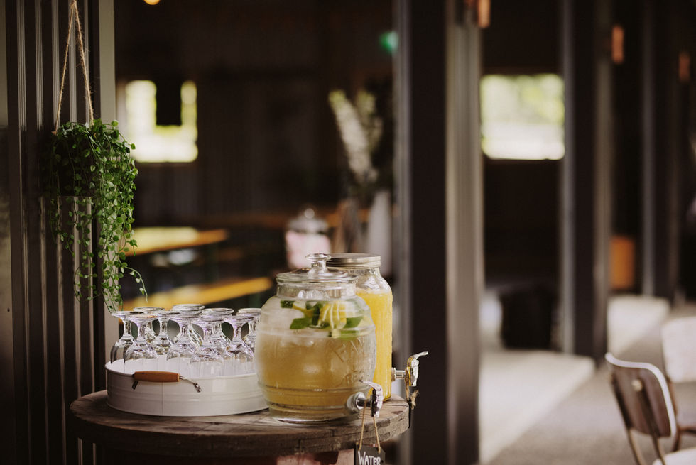 Drinks station with glass dispensers and stemware on a wooden barrel inside a dark-timbered barn