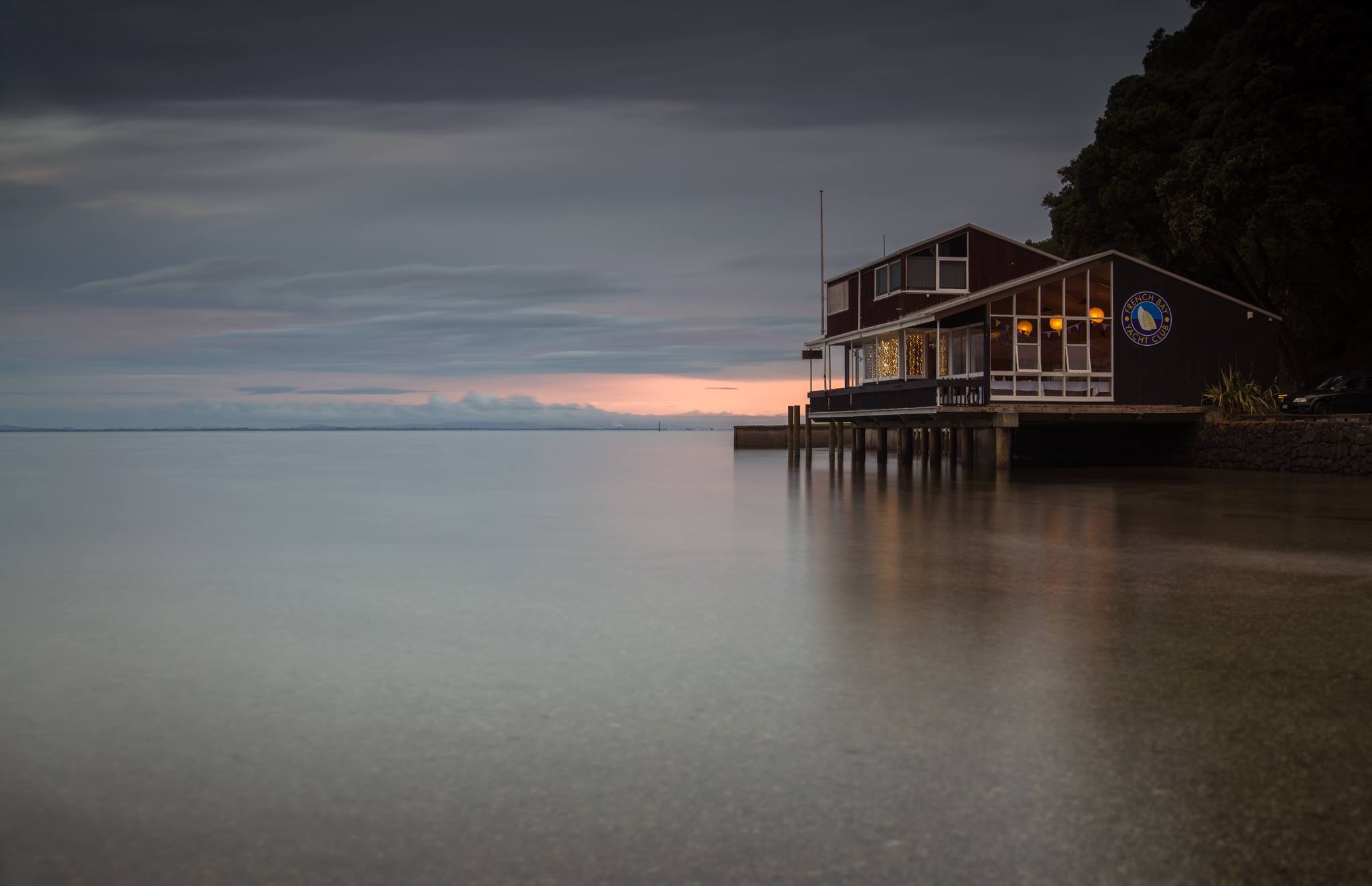 Timber clubhouse building on piles over water at dusk