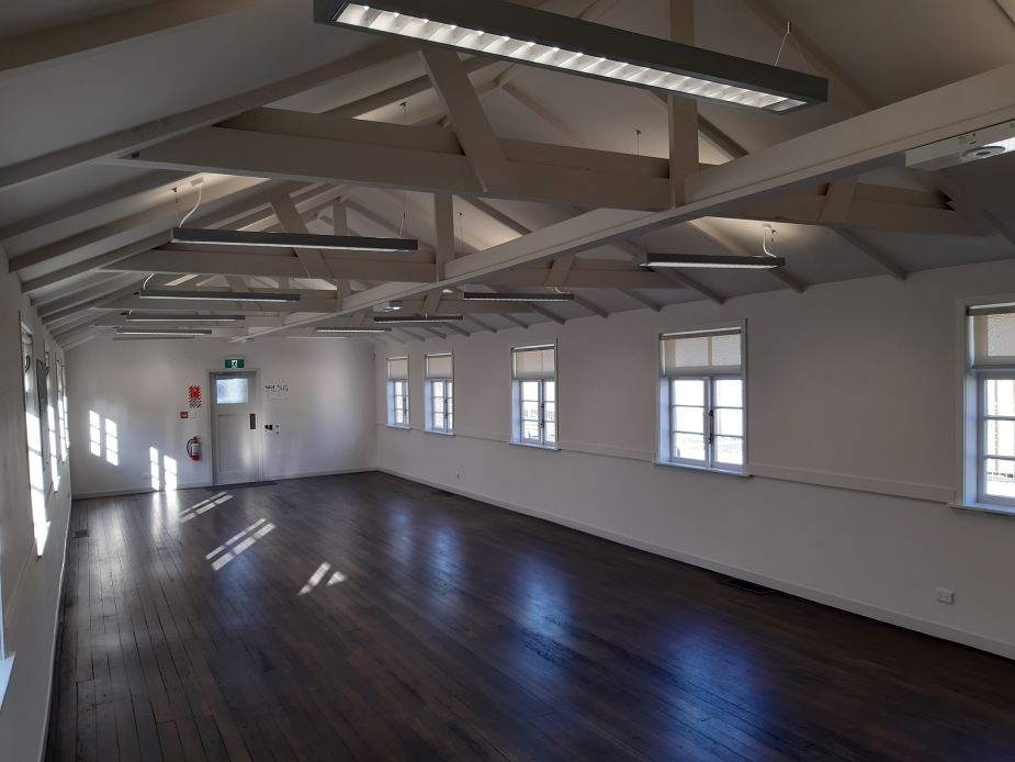 Large open event space with white walls, plasterboard panels, beige carpet, and stored equipment.