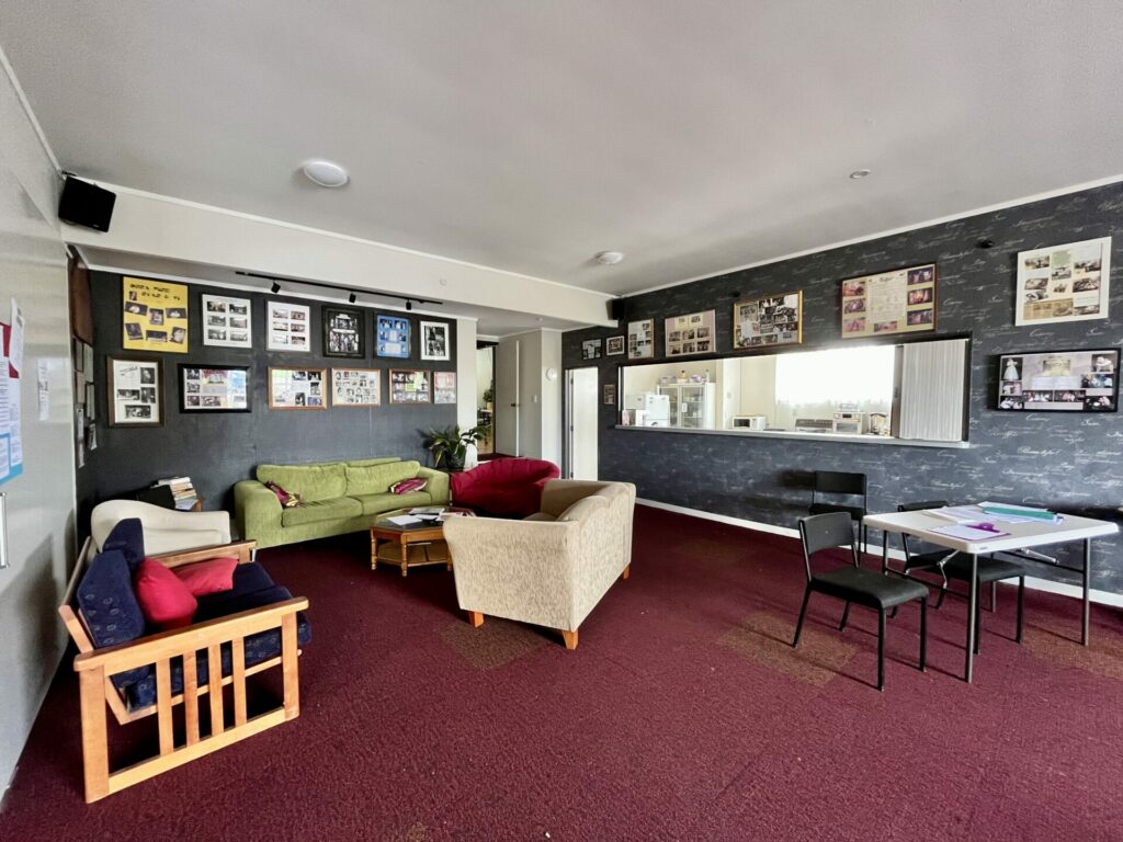 Green room lounge with mismatched sofas, chairs, notice boards and small bar window