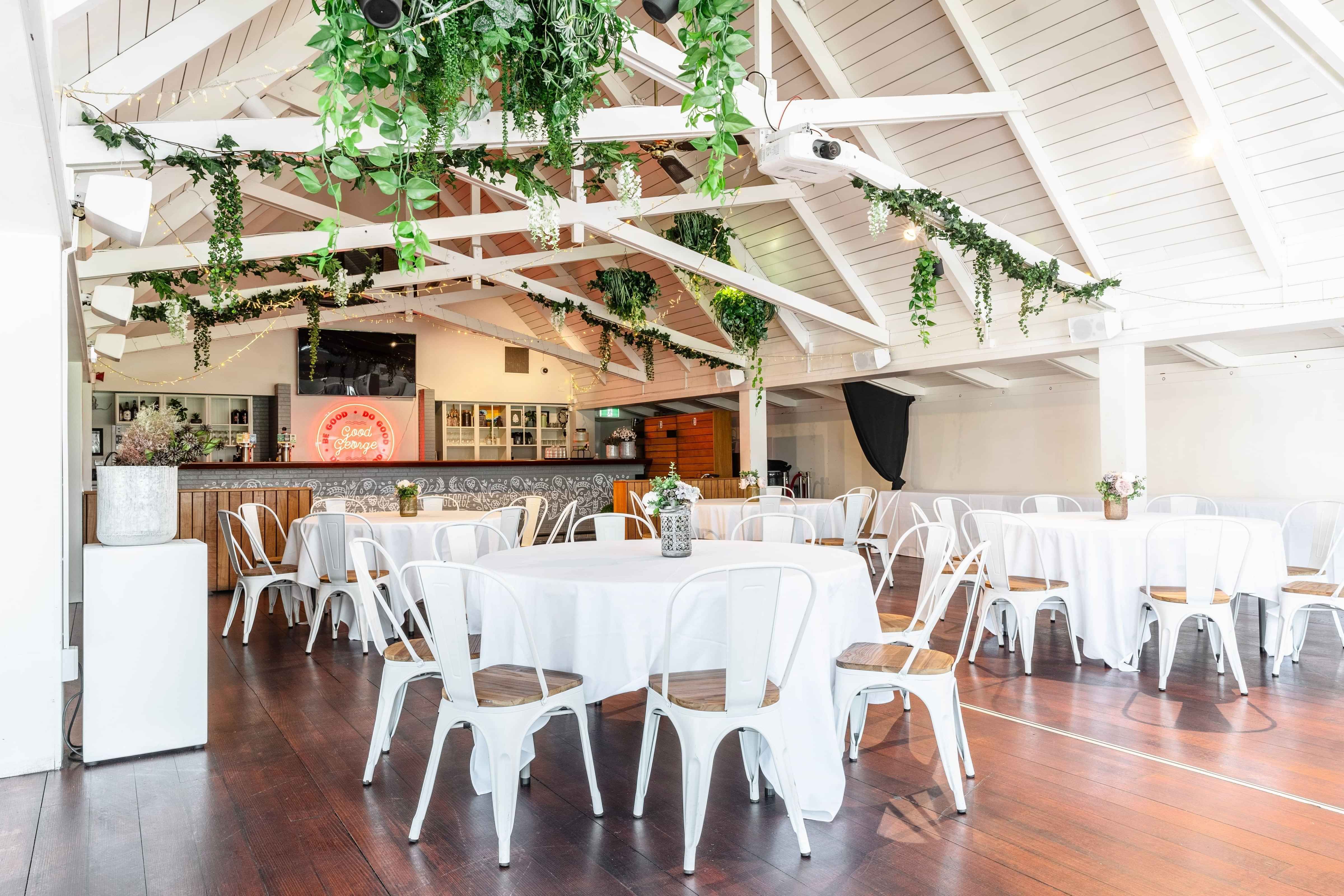 Open function space with exposed white trusses, hanging greenery and round tables set for event