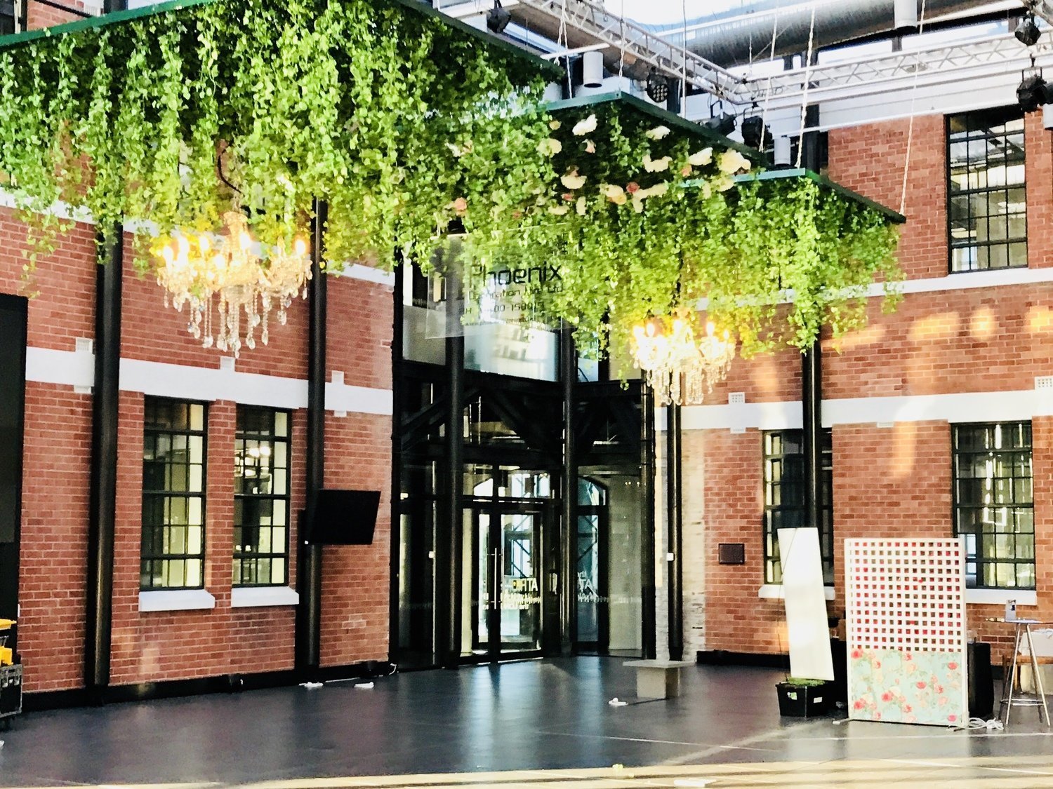 Industrial brick atrium interior with hanging greenery, chandeliers, and dark polished floor