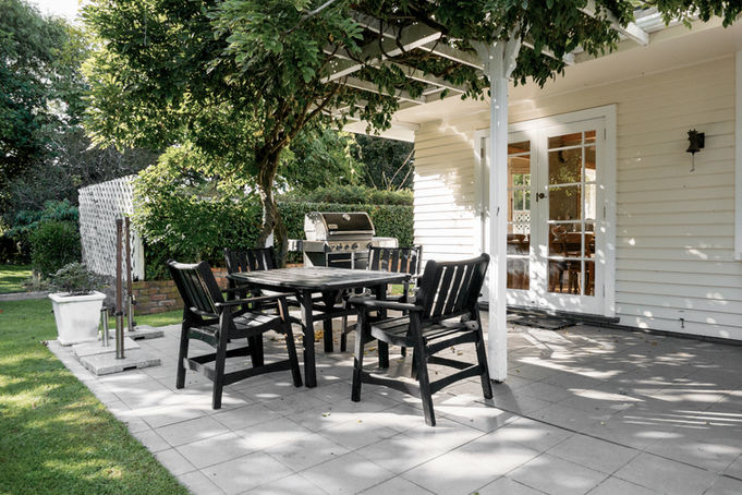 Paved patio and pergola alongside the white homestead with a garden outlook