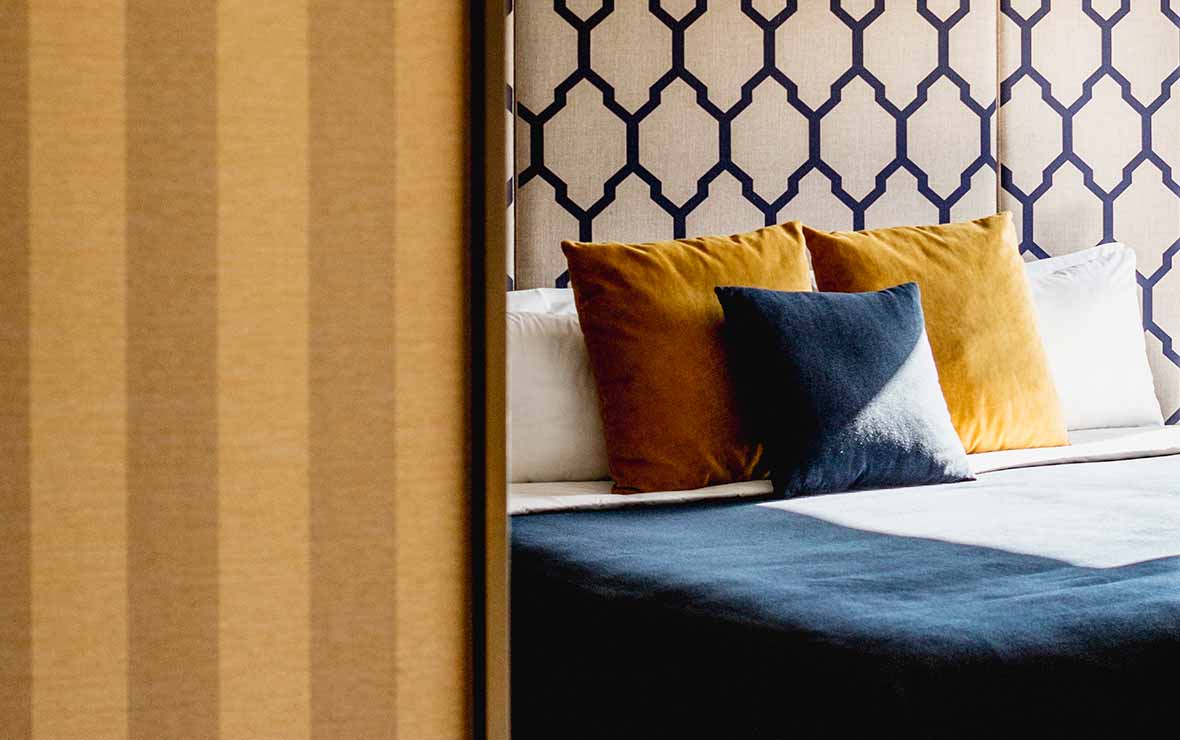 Hotel bed with patterned headboard and ochre cushions