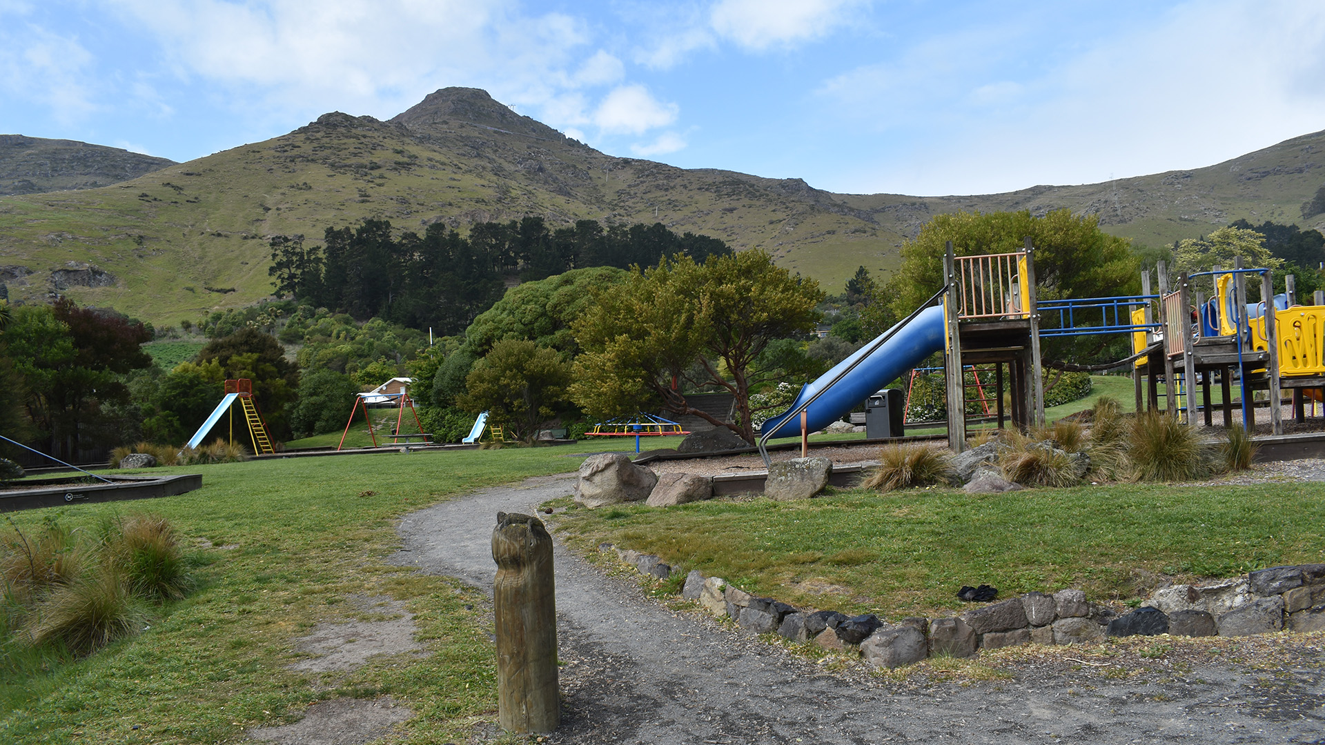 Park with playground equipment, trees, and hill backdrop