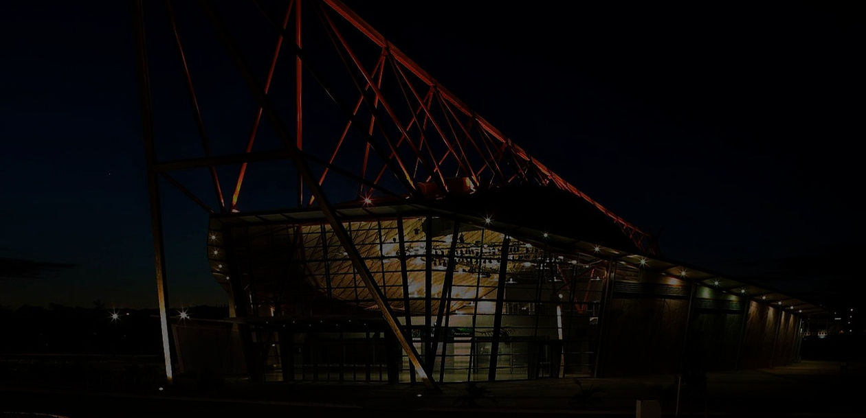 Dramatic event building at night with angled red steel lattice frame, glazed facade and exterior lighting