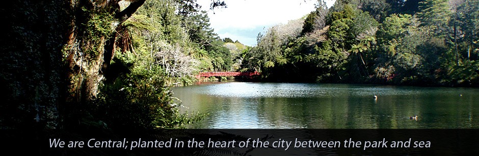 Tree-lined lake with red bridge viewed from foreground foliage, text overlay below