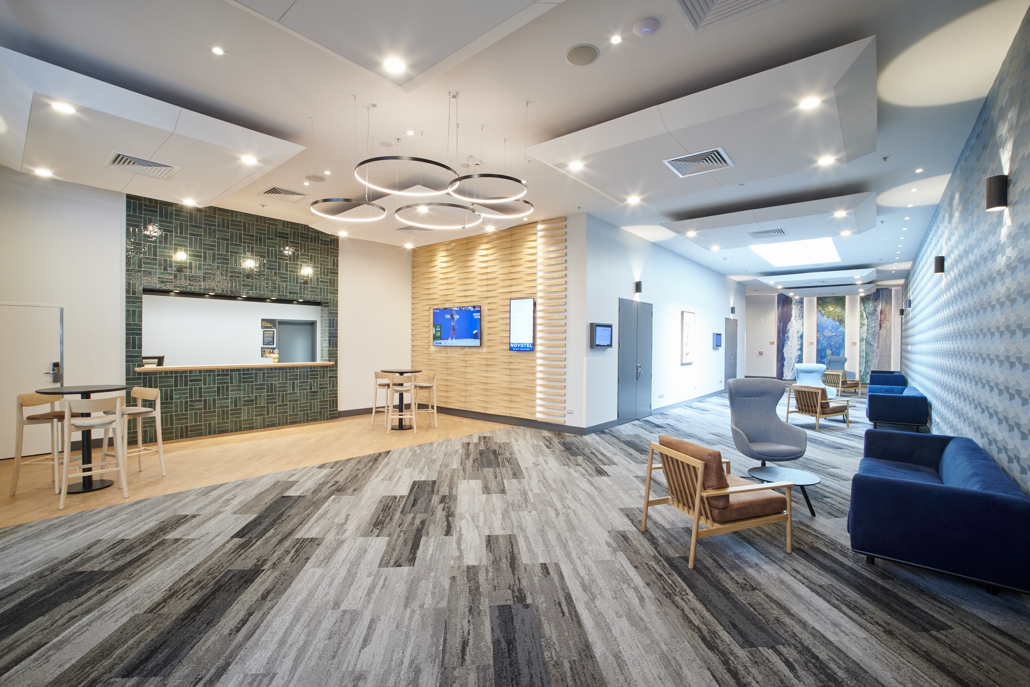 Contemporary hotel lobby with circular pendant lighting, tiled feature wall, striped carpet, and lounge seating