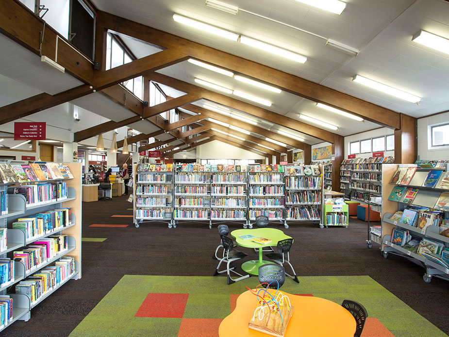 Library interior with bookshelves, exposed timber roof beams and children's furniture