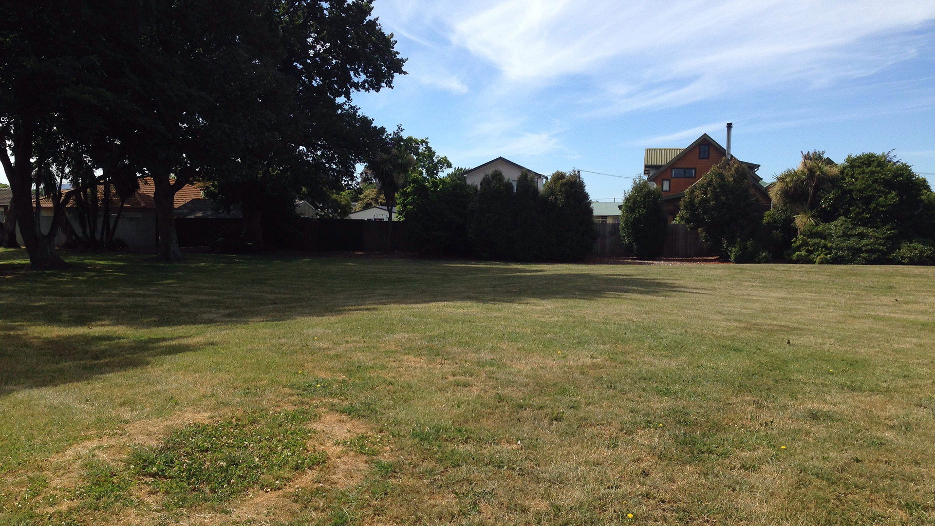 Open lawn area with trees at boundary and residential buildings beyond