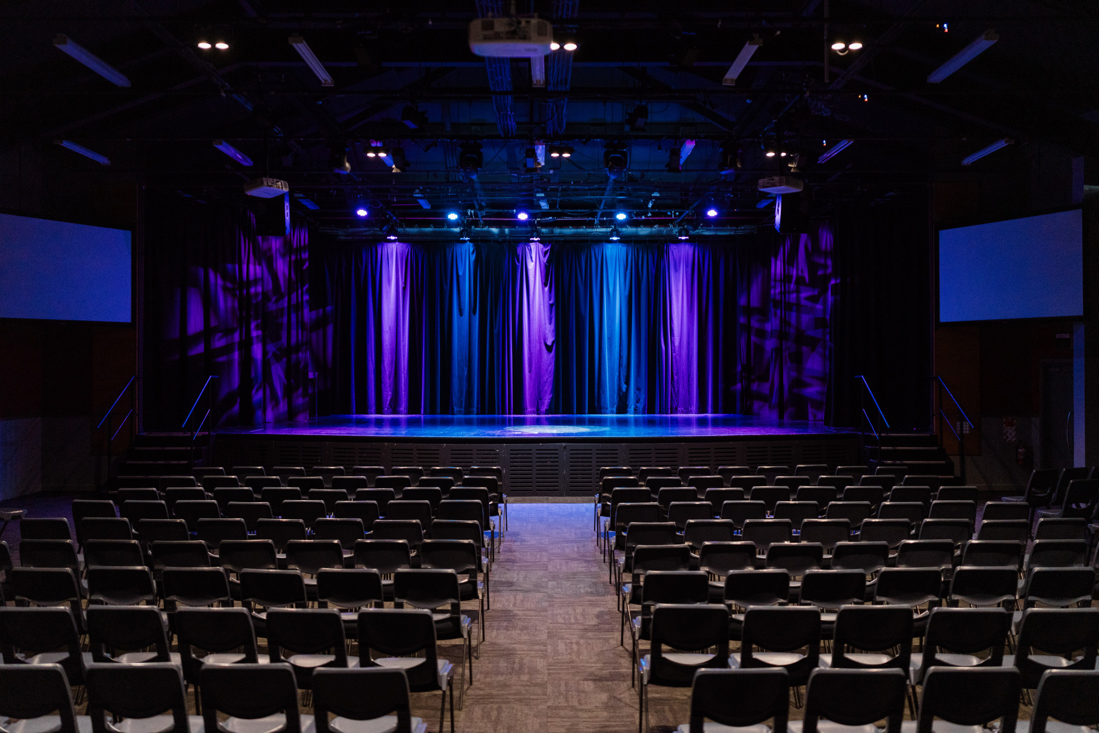 Large performing arts auditorium with stage, curtains lit in purple and blue, and rows of seats