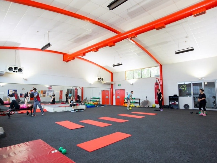 Fitness studio with red structural beams, mirrored wall and exercise mats on dark floor