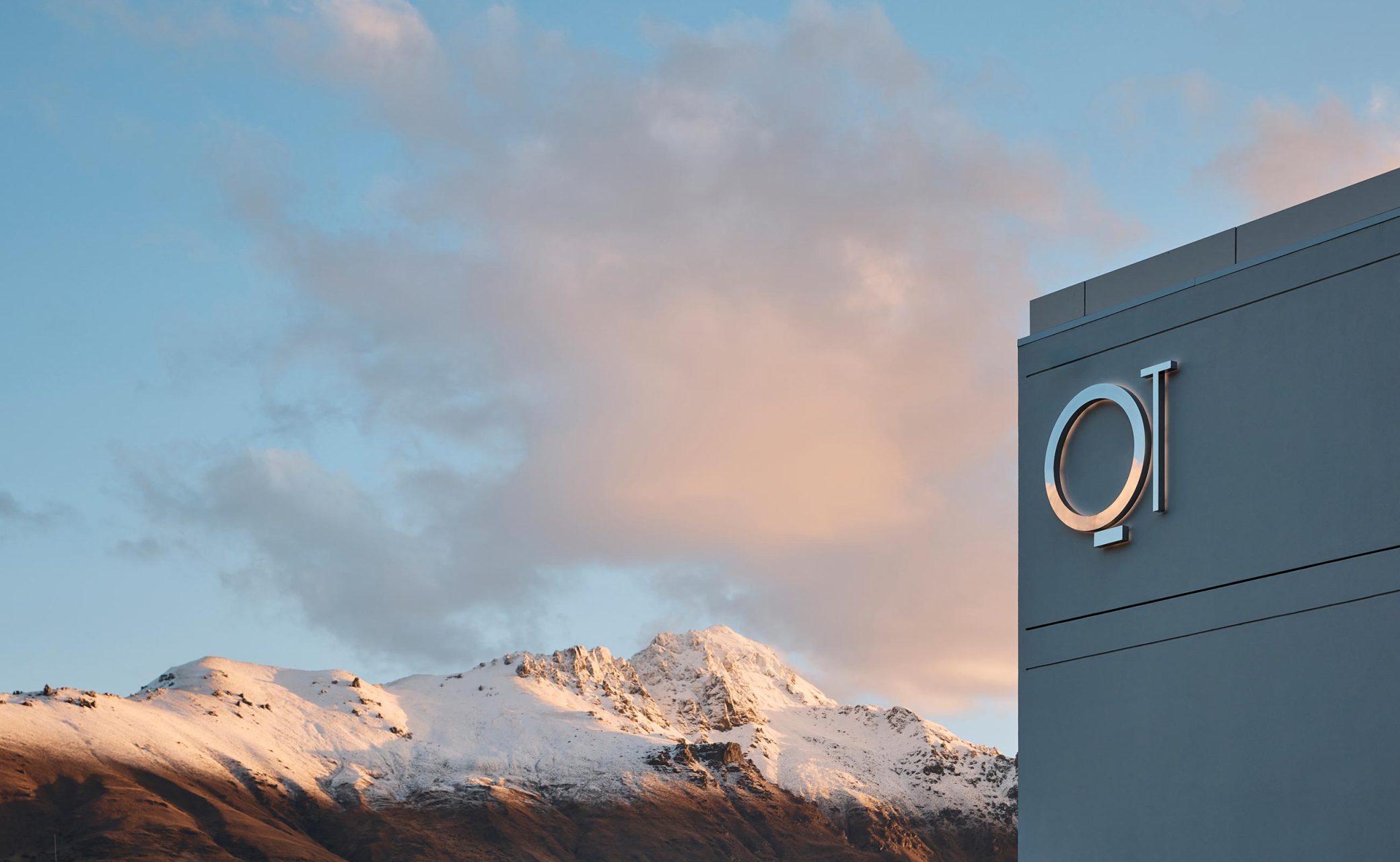 Grey rendered building exterior with brand signage, snow-capped mountains behind